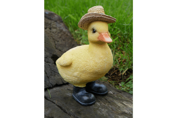 Cute rubber duck wearing a straw hat and black boots, standing outdoors on a wooden surface with green grass in the background.