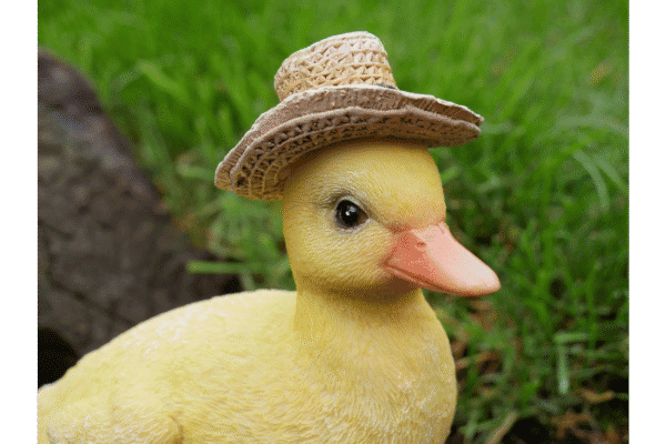 Cute yellow duck wearing a straw hat, sitting outdoors on green grass.