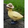 Decorative duck figurine wearing a straw hat, placed outdoors on a wooden surface with green grass in the background.
