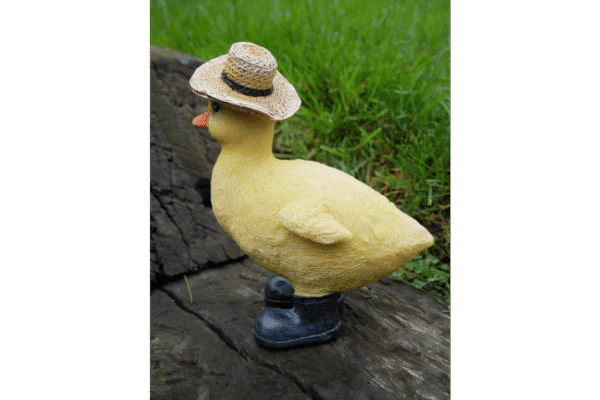 Decorative duck figurine wearing a straw hat, placed outdoors on a wooden surface with green grass in the background.