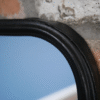 Close-up of a black mirror frame with a curved edge mounted on a textured brick wall.