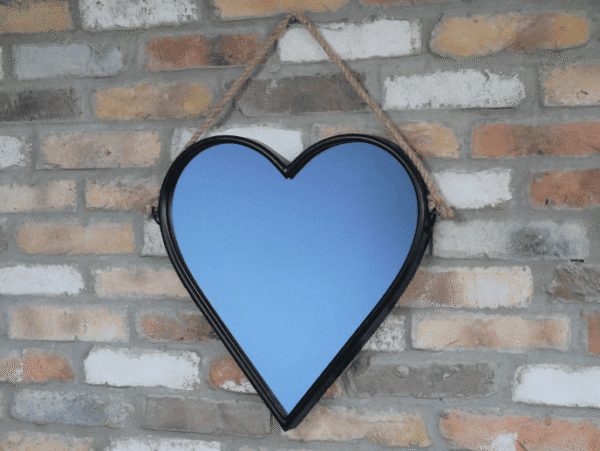 Heart-shaped mirror with a rope hanger against a brick wall, ideal for home decor.