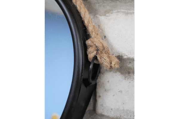 Close-up of a heart-shaped mirror with a rope hanging on a textured brick wall.
