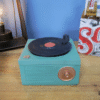 Vintage turquoise gramophone storage box with a black record on top, placed on a wooden surface.
