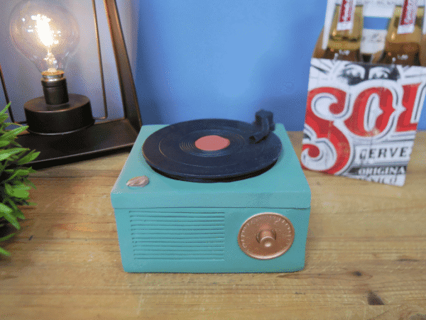 Vintage turquoise gramophone storage box with a black record on top, placed on a wooden surface.