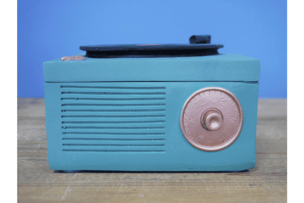 Vintage blue gramophone storage box with a round dial and black lid, placed on a wooden surface against a blue background.