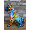 Colourful graffiti-style bulldog sculpture with vibrant patterns and bold colours, sitting on a wooden surface against a brick wall.