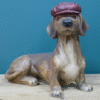 Decorative ceramic dog sculpture wearing a maroon cap, lying on a wooden surface against a blue background.