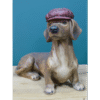 Decorative ceramic dog figurine wearing a textured maroon hat, sitting on a wooden surface against a teal background.