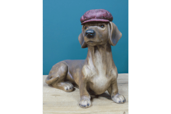 Decorative ceramic dog figurine wearing a textured maroon hat, sitting on a wooden surface against a teal background.