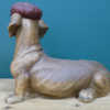 Unique dog-shaped decorative sculpture with a textured red hat, displayed on a wooden surface against a teal background.