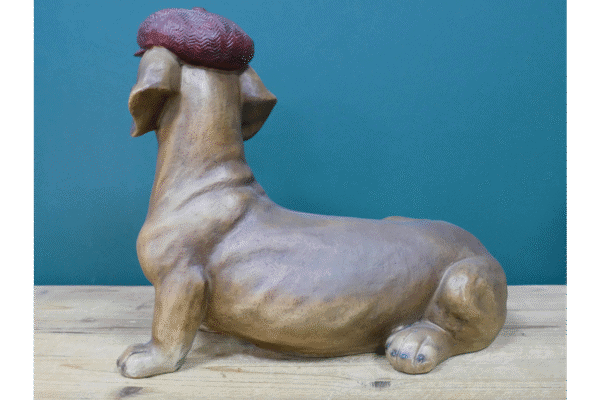 Unique dog-shaped decorative sculpture with a textured red hat, displayed on a wooden surface against a teal background.