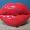 Red lips-shaped trinket box with glossy finish on a wooden surface against a blue background.