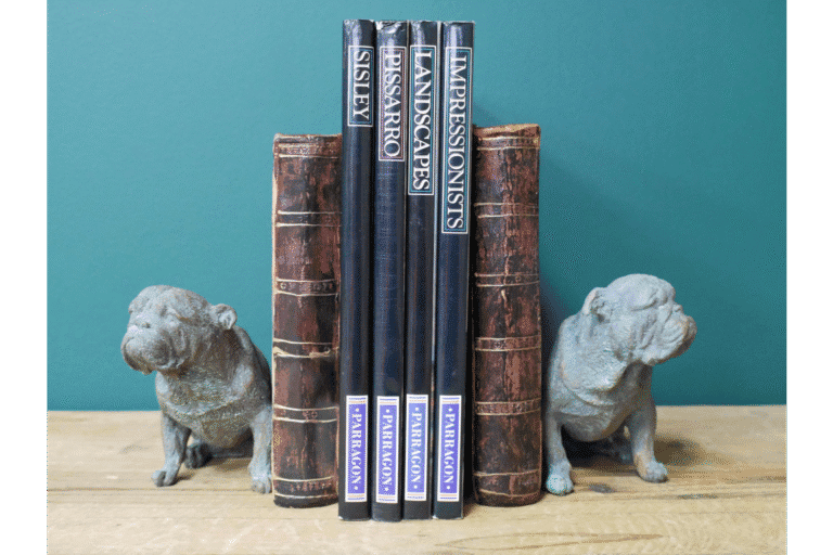 Decorative bulldog bookends holding a set of classic hardcover books on a wooden shelf against a teal background.