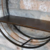 Industrial wall shelf unit with a mirror, featuring a black metal frame and a wooden shelf, mounted on a brick wall.