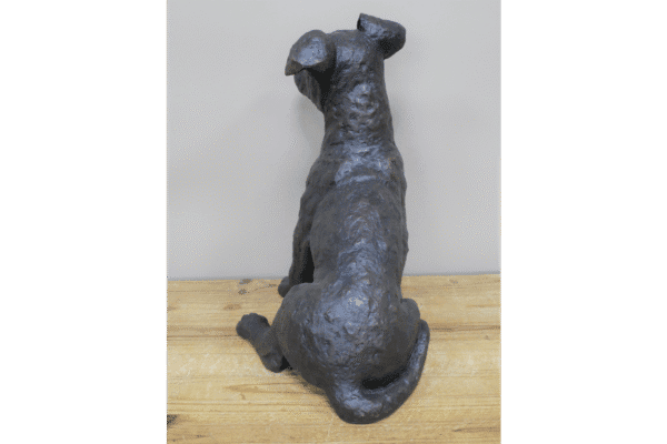 Gunmetal metallic sitting dog sculpture with a textured finish on a wooden surface.