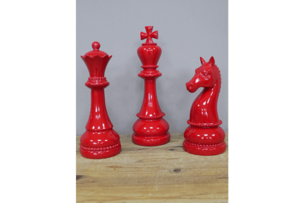 Red decorative chess pieces including a king, queen, and knight on a wooden surface.