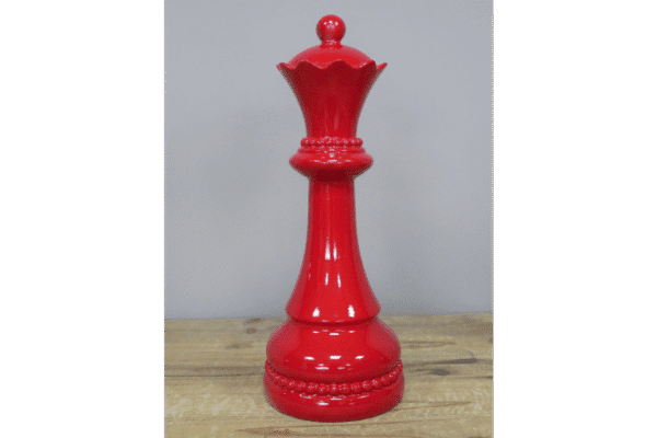 Red decorative chess queen piece made of glossy material, standing on a wooden surface.