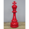 Red decorative chess king piece with a cross on top, placed on a wooden surface against a plain background.
