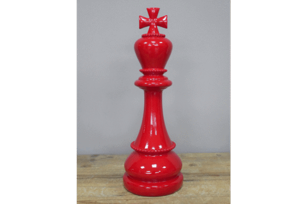 Red decorative chess king piece with a cross on top, placed on a wooden surface against a plain background.