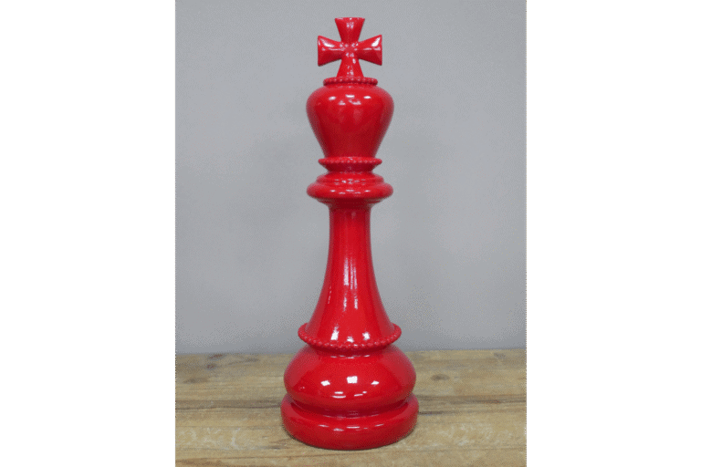 Red decorative chess king piece with a cross on top, placed on a wooden surface against a plain background.