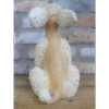 Sitting poodle plush toy with curly cream fur and a beige body, positioned against a brick wall.