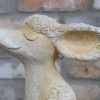 Decorative sculpture of a sitting poodle with detailed textured fur and a serene expression, placed against a brick wall background.