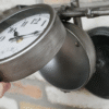 Close-up of a vintage-style bicycle handlebar clock mounted on a wall, with a black metal bell nearby, in a home decor setting.