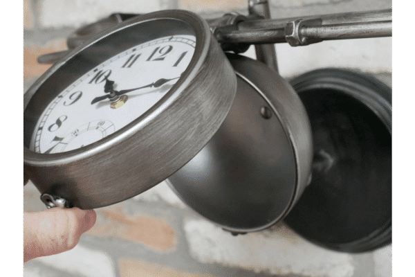Close-up of a vintage-style bicycle handlebar clock mounted on a wall, with a black metal bell nearby, in a home decor setting.
