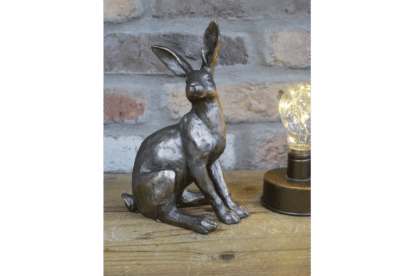 Decorative metallic sitting hare sculpture on wooden surface with brick wall background and warm light bulb.