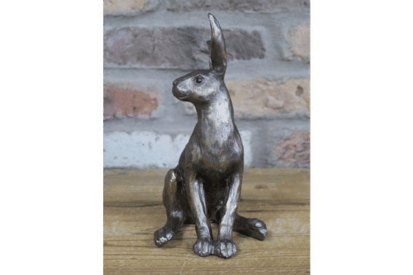 Decorative metal hare sculpture with a rustic finish, sitting on a wooden surface against a brick wall background.