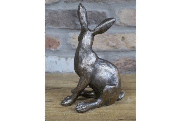 Decorative metallic rabbit sculpture sitting on a wooden surface against a brick wall background.