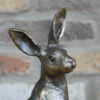 Decorative metal hare sculpture with tall ears against a brick wall background.