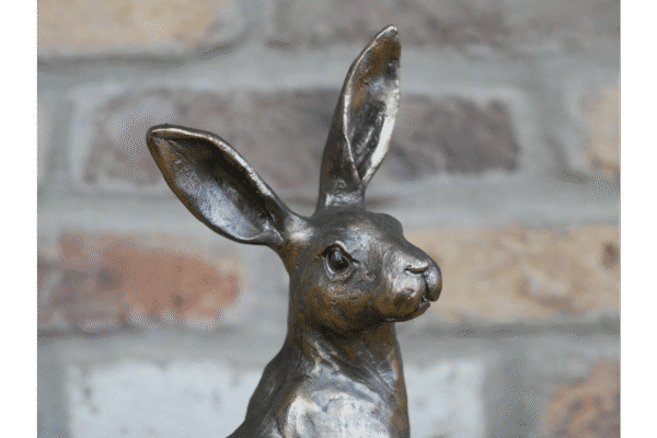 Decorative metal hare sculpture with tall ears against a brick wall background.