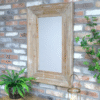 Wooden rectangular mirror with a rustic frame mounted on a brick wall, surrounded by green plants and decorative items.