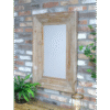 Wooden rectangular mirror with a rustic frame hanging on a brick wall, surrounded by green plants and a lantern.