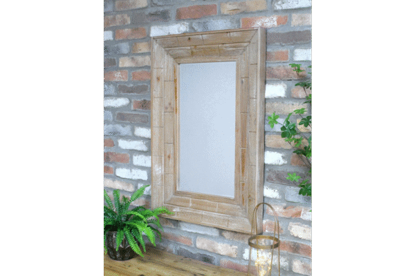 Wooden rectangular mirror with a rustic frame hanging on a brick wall, surrounded by green plants and a lantern.