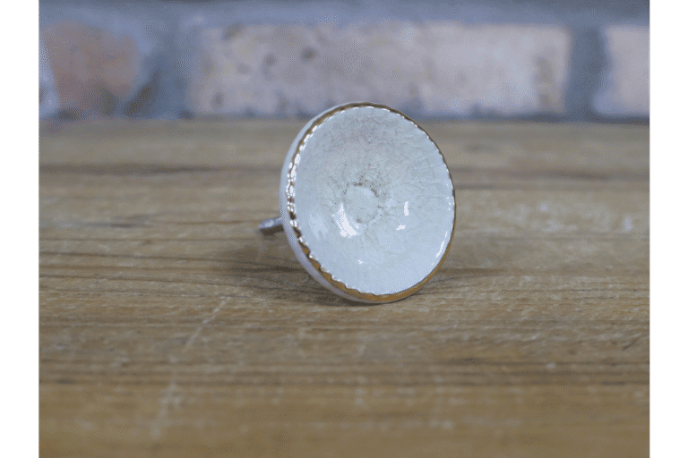 Ceramic pale green cabinet knob with gold trim on a wooden surface, suitable for home decorating projects.