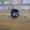 Close-up of a black ceramic cabinet knob with a glossy finish on a wooden surface.