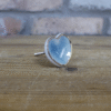 Ceramic pale blue heart-shaped cabinet knob with silver edging on a wooden surface.