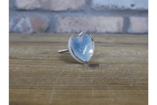 Ceramic pale blue heart-shaped cabinet knob with silver edging on a wooden surface.