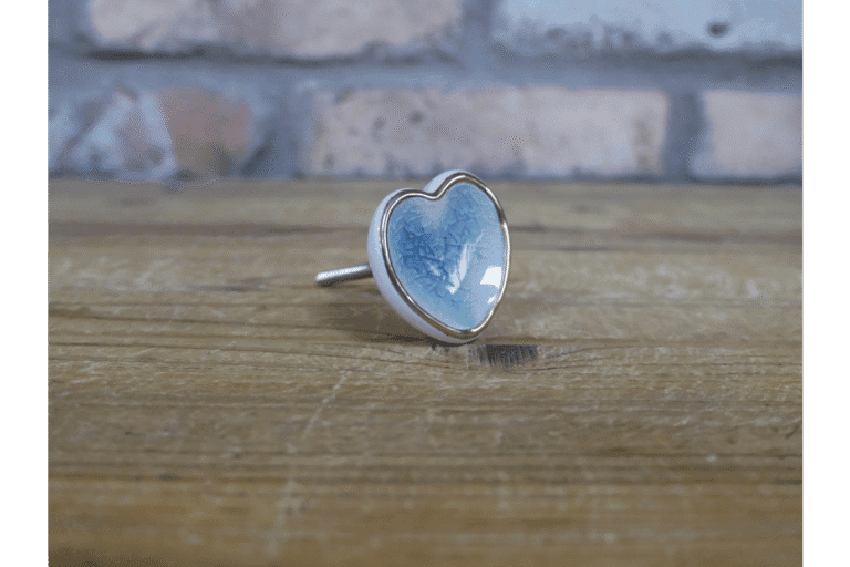 Ceramic pale blue heart-shaped cabinet knob with silver edging on a wooden surface.