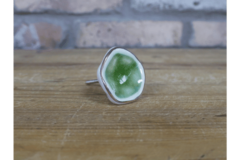Ceramic green cabinet knob with silver trim on a wooden surface, ideal for home decorating projects.