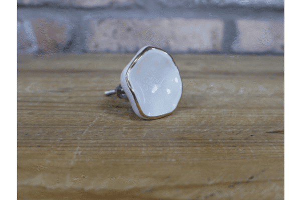 Ceramic off-white cabinet knob with gold trim on a wooden surface, suitable for home decorating projects.