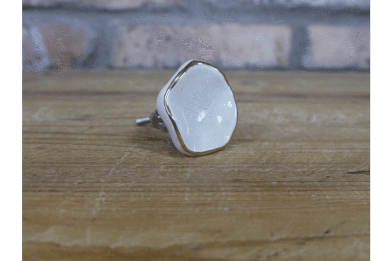 Ceramic off-white cabinet knob with gold trim on a wooden surface, suitable for home decorating projects.
