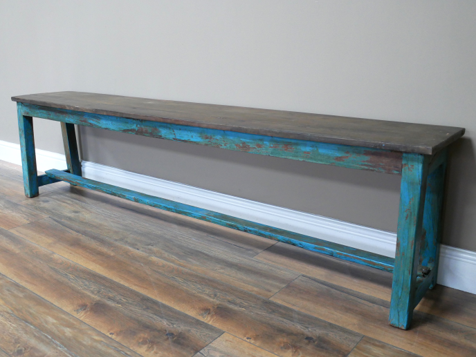 Blue distressed wooden bench with a rustic finish, placed against a plain grey wall on a wooden floor.