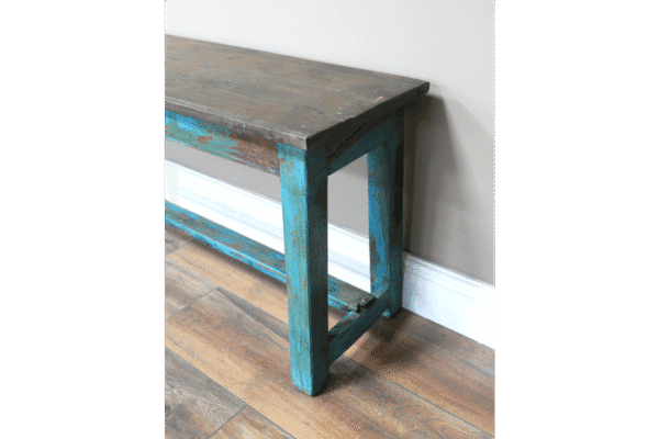 Blue distressed wooden bench with rustic finish, placed against a white wall on a wooden floor.