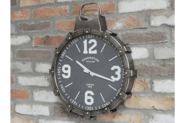 Industrial cog style clock with black face and white numerals, mounted on a brick wall, inspired by vintage railway station design.
