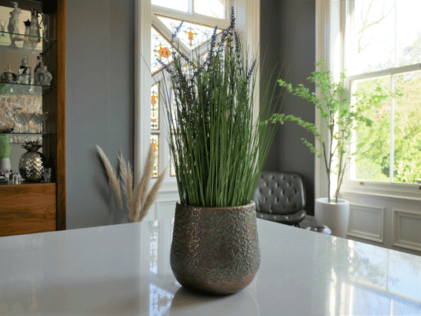 Decorative potted plant with tall green grass and purple flowers on a white table in a bright, modern room.