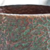 Close-up of a pitted aluminium planter with a textured, weathered surface in earthy tones.